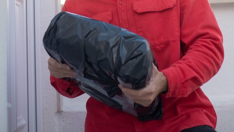A delivery man in a red uniform holds a package at a residential door, showcasing a typical delivery scene.